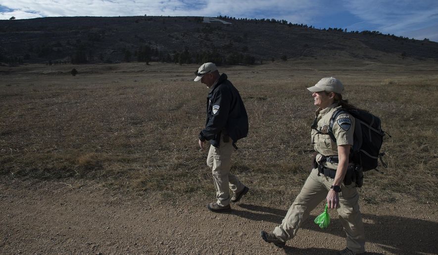In this Wednesday, Dec. 13, 2017 photo, Fort Collins lead ranger Dave Irwin, left, and senior lead ranger Kristin Powell head back to the parking lot after picking up garbage on the trail going past the old Hughes Stadium at Maxwell Natural Area in Fort Collins, Colo. (Timothy Hurst /The Coloradoan via AP)
