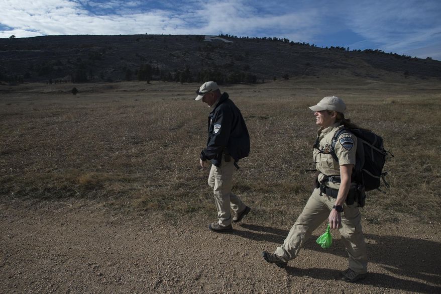In this Wednesday, Dec. 13, 2017 photo, Fort Collins lead ranger Dave Irwin, left, and senior lead ranger Kristin Powell head back to the parking lot after picking up garbage on the trail going past the old Hughes Stadium at Maxwell Natural Area in Fort Collins, Colo. (Timothy Hurst /The Coloradoan via AP)
