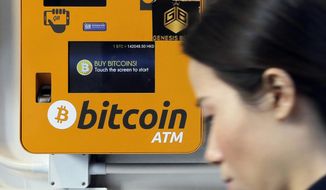In this Dec. 21, 2017 file photo, a woman walks past the Bitcoin ATM in Hong Kong. (AP Photo/Kin Cheung, File) **FILE**