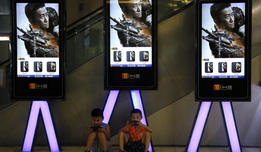 FILE - In this Aug. 10, 2017, file photo, children use smartphones near monitors displaying Chinese action movie "Wolf Warrior 2" at a cinema in Beijing. China's total domestic movie ticket sales rose 13.5 percent in 2017 to 55.9 billion yuan ($8.6 billion), a state news agency said Monday, Jan. 1, 2018. The top-grossing title was the mainland-made action picture "Wolf Warrior 2," which took in 5.7 billion yuan ($875 million), the Xinhua News Agency said, citing data from the State Administration of Press, Publication, Radio, Film and Television. (AP Photo/Andy Wong, File)