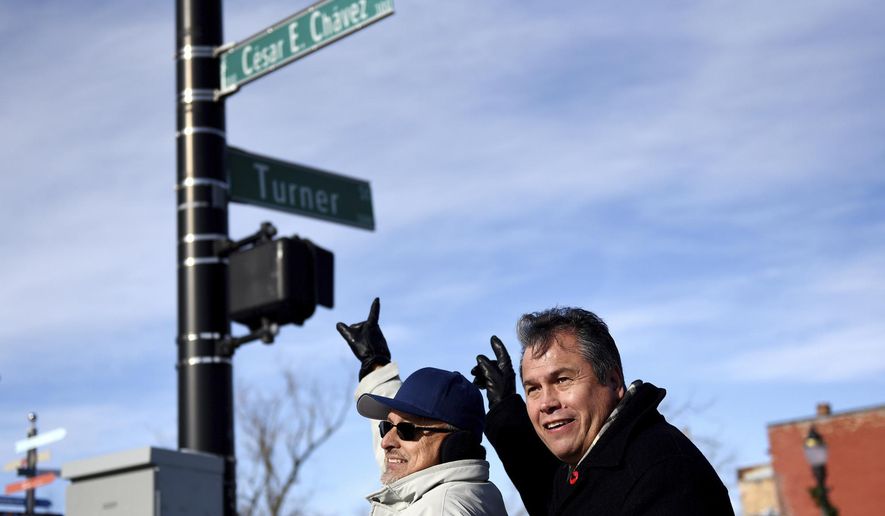 Guillermo Lopez, left, and Andy Garza point to the Cesar E. Chavez Avenue sign while posing for a photograph during an unveiling ceremony to mark the changing of Grand River Avenue to Cesar E. Chavez Avenue on Tuesday, Jan. 2, 2018, at the intersection of Cesar E. Chavez Avenue and Turner Street in Old Town Lansing, Mich. (Nick King/Lansing State Journal via AP)