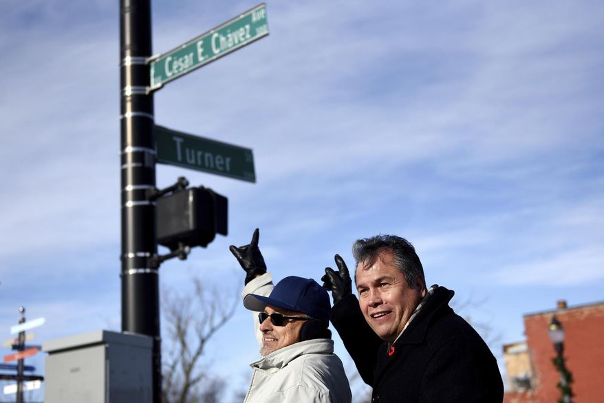 Guillermo Lopez, left, and Andy Garza point to the Cesar E. Chavez Avenue sign while posing for a photograph during an unveiling ceremony to mark the changing of Grand River Avenue to Cesar E. Chavez Avenue on Tuesday, Jan. 2, 2018, at the intersection of Cesar E. Chavez Avenue and Turner Street in Old Town Lansing, Mich. (Nick King/Lansing State Journal via AP)