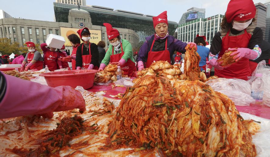 FILE - In this Nov, 3. 2017, file photo, women make kimchi, a traditional fermented South Korean pungent vegetable dish, to donate to needy neighbors in preparation for the winter season during Kimchi Festival at Seoul City Hall Plaza in Seoul, South Korea. Spicy, pungent kimchi; thick fermented soups filled with meat so tender it falls off the bone; barbecued everything; all of it washed down with ubiquitous soju liquor. (AP Photo/Ahn Young-joon, File)