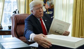 President Donald Trump grabs a box containing the tax bill after signing it in the Oval Office of the White House, Friday, Dec. 22, 2017, in Washington. (AP Photo/Evan Vucci)