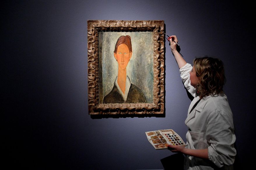 In this photo taken on March 15, 2017, a woman puts the finishing touches on the painting Ritratto di Chaim Soutine ' (Portrait of Chaim Soutine), attributed in the exhibit to the Italian painter Amedeo Modigliani, on display at the Ducal Palace in Genoa, Italy. Consumer advocates are demanding refunds after an expert ruled that a Genoa exhibit was full of Modigliani fakes. The Italian news agency ANSA reported Tuesday that the expert, appointed by a Genoa court during a prosecutor’s probe, concluded that at least 20 of 21 paintings displayed in 2017 during the Ducal Palace exhibit were clearly fakes. (Luca Zennaro/ANSA via AP)