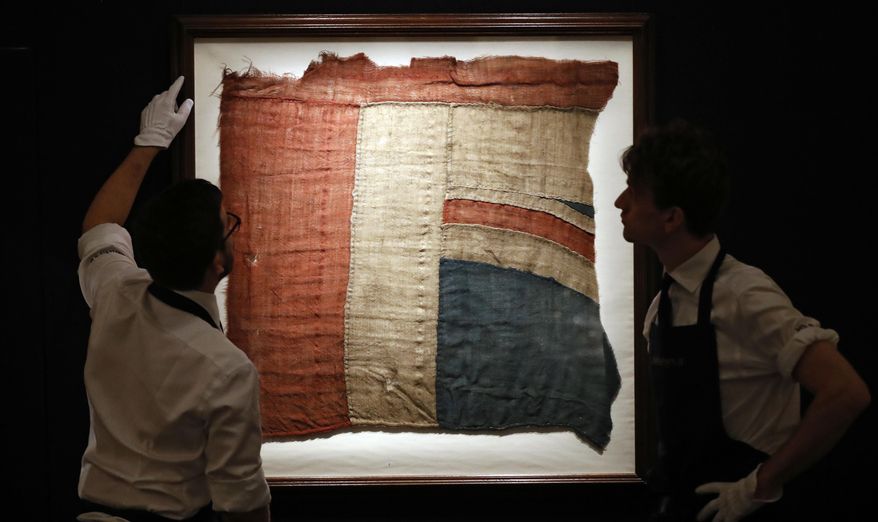 Sotheby's employees look at a frame with a fragment of a Union Jack in London, Thursday, Jan. 11, 2018. An exceptionally large fragment of the Union Flag, which flew from HMS Victory at the Battle of Trafalgar and Love Letters of Britain's Hero, Lord Nelson, to his famous mistress, Lady Hamilton shedding light on the liaison that scandalised 18th-century in England are on auction at Sotheby's. (AP Photo/Frank Augstein)
