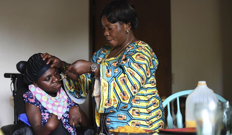 In this Aug. 10, 2017 photo, Binwa Masoka, right, feeds her daughter Moshi Masoka, in their home in Corvallis, Ore. A childhood illness acquired in the Tanzania refugee camp where she was born left Moshi unable to walk, speak or feed herself. Binwa, 43, is paid by the state to be Moshi’s full-time caregiver, and she’s taking classes in English and computer literacy through Linn-Benton Community College. (Anibal Ortiz/The Corvallis Gazette-Times via AP)