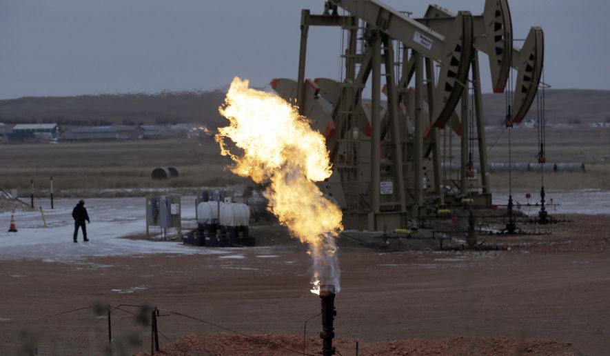 FILE - In this Oct. 22, 2015, file photo, workers tend to oil pump jacks behind a natural gas flare near Watford City, N.D. Fearing sanctions by the state, some North Dakota oil drillers have begun cutting output to control the amount of natural gas that's being burned off at well sites and wasted as a byproduct of crude production, industry and state officials say. (AP photo/Eric Gay, File)