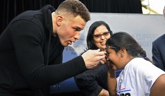 Los Angeles Clippers&#x27; Blake Griffin puts glasses on a student as Los Angeles Unified School District school board president Monica Garcia watches at Lovelia P. Flournoy Elementary School, Tuesday, Jan. 16, 2018, in the Nickerson Gardens area of Los Angeles, where the Clippers announced a partnership with Vision to Learn and the Los Angeles Unified School District to provide students with eyeglasses. Over 600,000 students will benefit from the program. (AP Photo/Mark J. Terrill)
