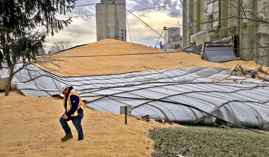An AT&T worker walks through thousands of bushels of corn that cover Ohio Route 571 Monday, Jan. 22, 2018, after a grain bin at Miami Valley Feed and Grain collapsed on Sunday evening in New Carlisle, Ohio. Emergency personnel were still assessing the scene Monday morning. (Bill Lackey/Dayton Daily News via AP)