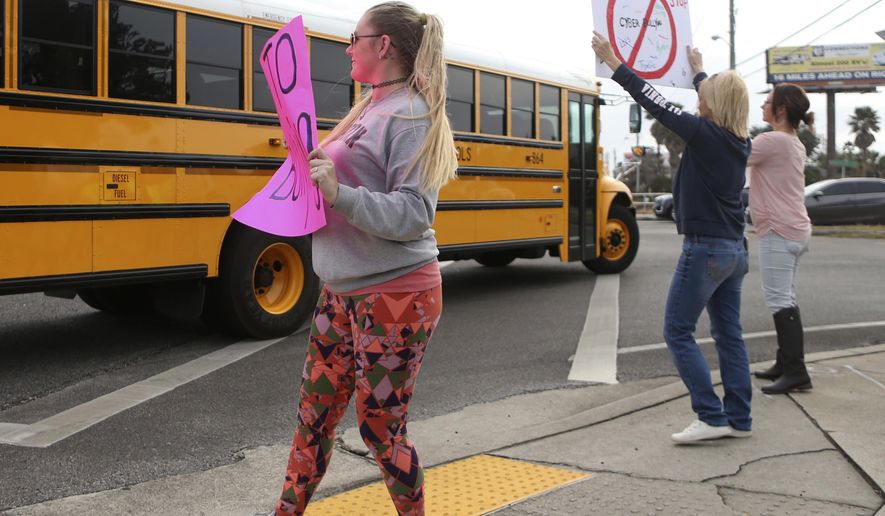 In this Monday, Jan. 22, 2018 photo, Kelli Martin, left, holds a sign with "Say No to Bullying" written across it as a school bus drives past during a protest by concerned parents and family members against bullying near Surfside Middle School, in Panama City Beach, Fla. Two 12-year-olds in Florida have been charged with cyberstalking in connection with the death of a student at the middle school, who police say hanged herself two weeks ago. (Patti Blake/News Herald via AP)