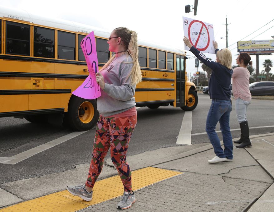 In this Monday, Jan. 22, 2018 photo, Kelli Martin, left, holds a sign with "Say No to Bullying" written across it as a school bus drives past during a protest by concerned parents and family members against bullying near Surfside Middle School, in Panama City Beach, Fla. Two 12-year-olds in Florida have been charged with cyberstalking in connection with the death of a student at the middle school, who police say hanged herself two weeks ago. (Patti Blake/News Herald via AP)