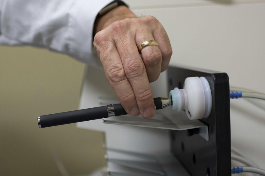 FILE - In this Thursday, Nov. 10, 2016 file photo, a doctor holds an e-cigarette in a smoking lab at the Centers for Disease Control and Prevention in Atlanta. An exhaustive government report issued Tuesday, Jan. 23, 2018 wrestles with the potential benefits and harms of the vapor-emitting devices, which remain unclear more than a decade after their introduction in the U.S. (AP Photo/Branden Camp)