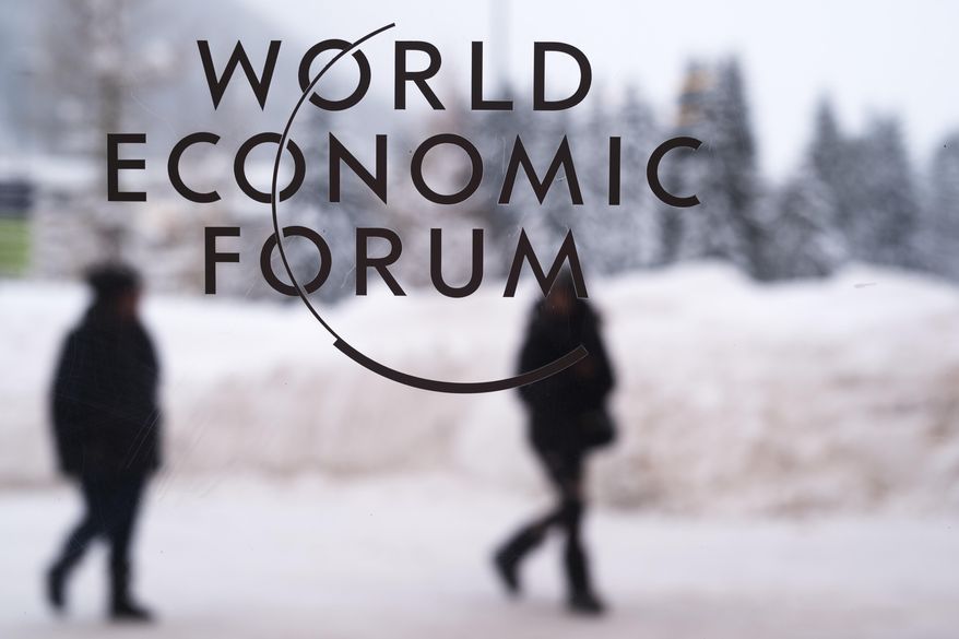 Two persons walk behind the logo of the World Economic Forum at the meeting's conference center in Davos, Switzerland, Sunday, Jan. 21, 2018. One question looms as President Donald Trump packs his bags and heads for the mountains of Switzerland later this week: How will the diet Coke-loving nationalist fit in with the champagne-swilling globalists he’ll encounter at the World Economic Forum in Davos? (AP Photo/Markus Schreiber)