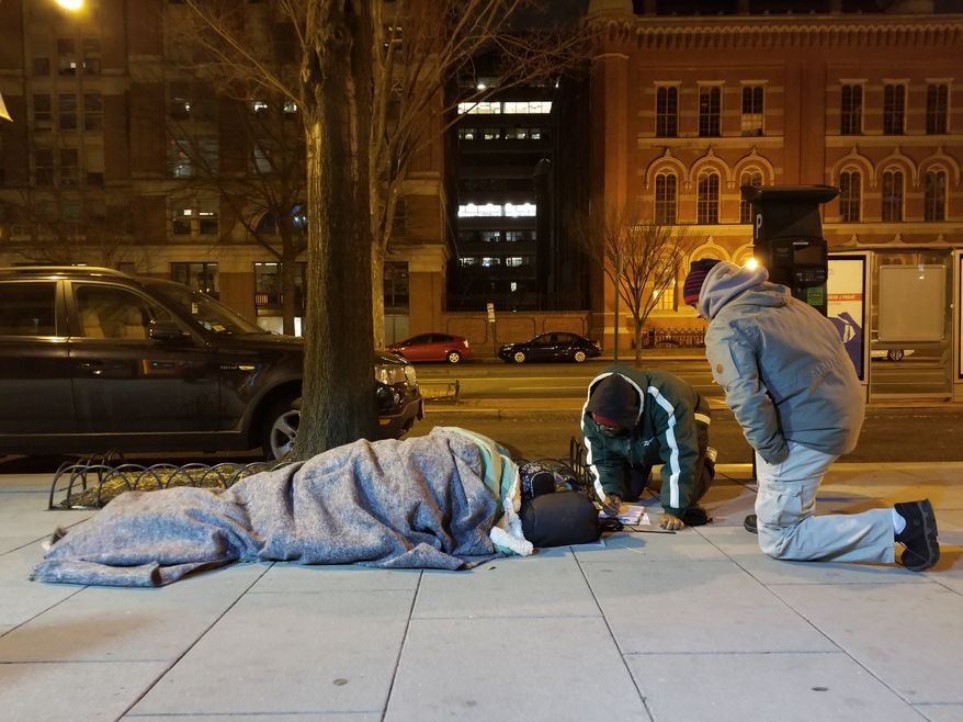 Hector Lugo, right, and Kevin Morton, left, kneel by a bus stop as they survey a homeless man Wednesday night for the annual Point-In-Time census of homelessness in the District. (Julia Airey/The Washington Times). **FILE**