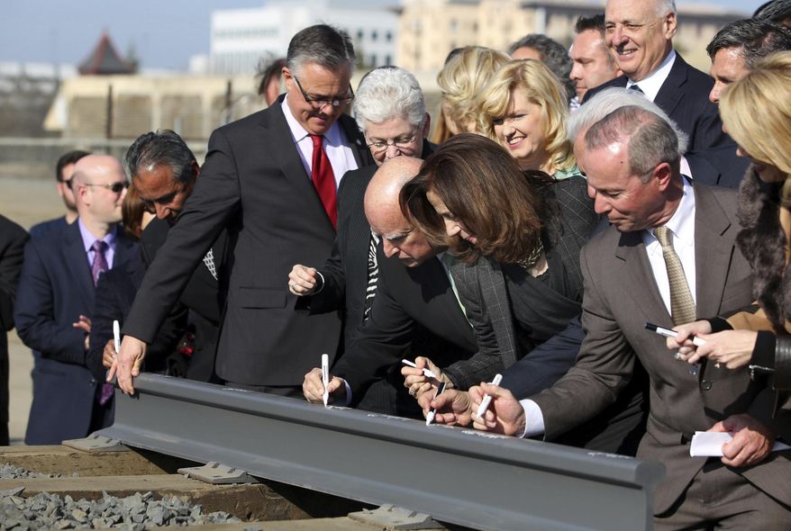 FILE - In this Jan. 6, 2015, file photo, Gov. Jerry Brown, center, and his wife, Anne Gust Brown, fourth from right, sign a portion of a rail at the California High-Speed Rail Authority groundbreaking event as Gina McCarthy, administrator of the U.S. Environmental Protection Agency, standing next to Brown at left, watches in Fresno, Calif. A bipartisan team of lawmakers are seeking a formal audit of California's high-speed rail project following a nearly $3 billion jump in costs. Democratic Sen. Jim Beall and Republican Assemblyman Jim Patterson will make their pitch for the audit Tuesday, Jan. 30, 2018, to a joint committee that will choose whether to authorize it. (AP Photo/Gary Kazanjian, File)