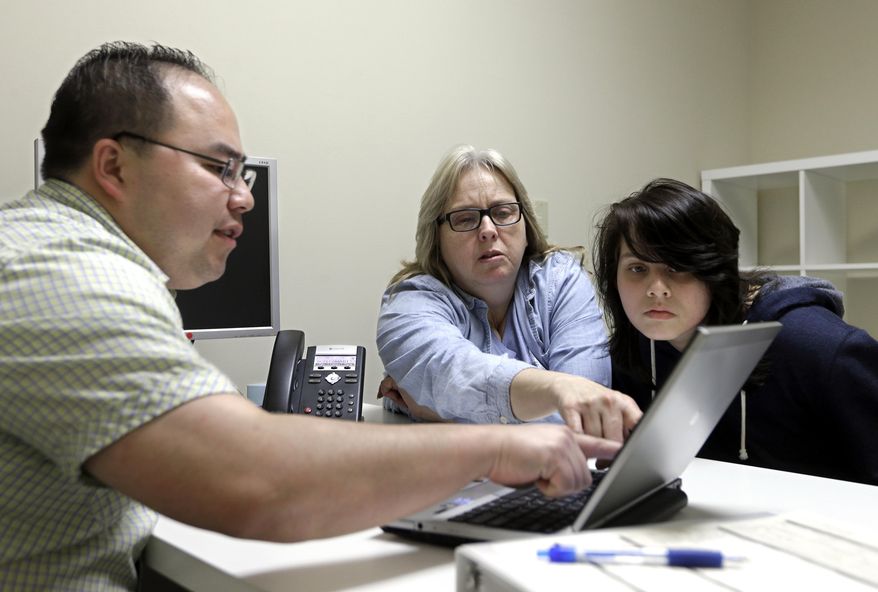 FILE - In this Feb. 12, 2015, file photo, Enrollment counselor Vue Yang, left, goes over some of the health insurance plans available to Laura San Nicolas, center, accompanied by her daughter, Geena, 17, while enrolling for health insurance at Sacramento Covered in Sacramento, Calif. Enrollment in Cover California dropped slightly this year as about 35,000 fewer people signed up for coverage through the state's insurance marketplace. Cover California executive director Peter Lee says some of the decline is because some people who make too much to qualify for subsides could get a better deal elsewhere. (AP Photo/Rich Pedroncelli, file)