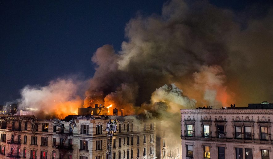 FILE - In this Nov. 17, 2017 file photo, people wait in their apartments as firefighters battle a large fire on the top floors of an apartment building in New York City's Harlem neighborhood. On Friday, Feb. 9, 2018, Jelani Parker, a man who lived in the building at the time of the blaze, pleaded not guilty to charges of arson, assault and reckless endangerment. He was ordered held without bail. (AP Photo/Andres Kudacki, File)