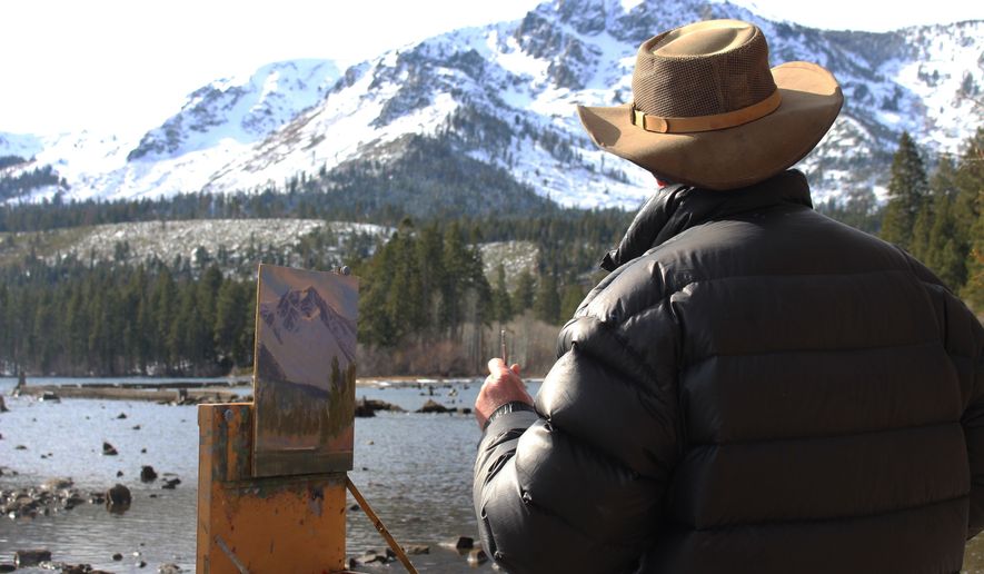In a Monday, Jan. 22, 2018 photo, artist Charles Muench paints the view of Mount Tallac from a beach at Fallen Leaf Lake in South Lake Tahoe, Calif., creating a piece he calls “Clouds Clearing – Mt. Tallac.” (Claire Cudahy/The Tahoe Tribune via AP)