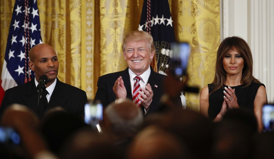 President Donald Trump, center, and first lady Melania Trump, right, applaud as Surgeon General Jerome Adams, left, speaks during the National African American History Month reception in the East Room of the White House in Washington, Tuesday, Feb. 13, 2018. (AP Photo/Carolyn Kaster)