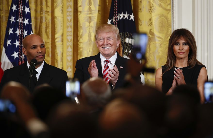 President Donald Trump, center, and first lady Melania Trump, right, applaud as Surgeon General Jerome Adams, left, speaks during the National African American History Month reception in the East Room of the White House in Washington, Tuesday, Feb. 13, 2018. (AP Photo/Carolyn Kaster)