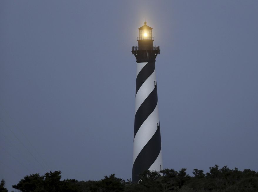 FILE - In this July 3, 2014, file photo, the Cape Hatteras Lighthouse shines on Hatteras Island, N.C., before dawn. The lighthouse has gone dark for about a month while officials await custom-made parts for storm damage repairs. Petty Officer 3rd Class Nate Cox, a U.S. Coast Guard spokesman, said Tuesday, Feb. 13, 2018, the light has been off since mid-January after machinery was damaged by storms. (Steve Earley/The Virginian-Pilot via AP, File)