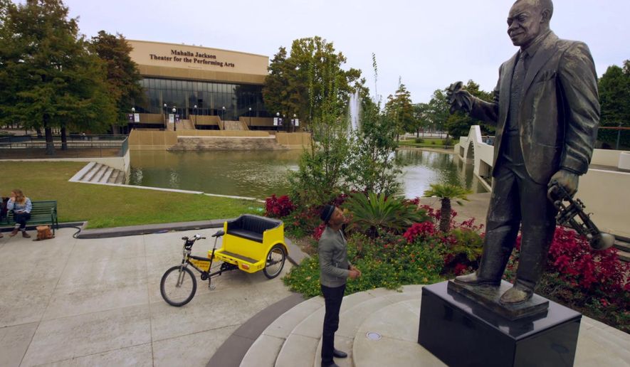 This undated image taken from video and provided by Brand USA is from the new IMAX movie called "America's Musical Journey" and shows musician Aloe Blacc in New Orleans looking at a statue of the late Louis Armstrong. The movie premieres Thursday, Feb. 15, 2018, and was produced by Brand USA, the agency that markets the U.S. to the rest of the world, along with MacGillivray Freeman Films. The movie follows Blacc as he travels around the U.S., learning about the musical heritage and genres of music associated with various cities. (Brand USA via AP)