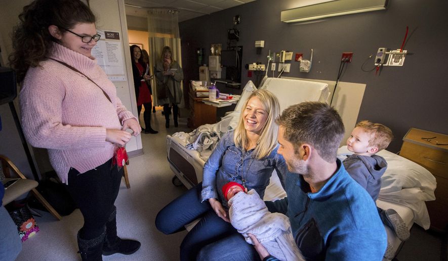 In this Jan. 29, 2018 photo, Zaia Wilcoxon, left, visits Dan And Tara Ballard, holding their one-day-old daughter Nora, with their son, Charlie, in Peoria, Ill. Zaia gave parents tiny, knitted red hats as part of the American Heart Association event "Little Hats, Big Hearts" to recognize moms and babies, encouraging them to live heart healthy lives. Zaia herself was born with a heart condition that wasn't discovered until she was two. Her mother, Annessa Wilcoxon, helped crochet two hats, adding to what officials said were donated hats from all across the state. Hats were distributed at both OSF Saint Francis Medical Center and the adjoining Children's Hospital of Illinois. (Fred Zwicky/Journal Star via AP)