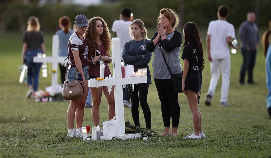 People pay homage at the memorial crosses for the 17 deceased students and faculty from the Wednesday shooting at Marjory Stoneman Douglas High School, in Parkland, Fla., Friday, Feb. 16, 2018. Nikolas Cruz, a former student, was charged with 17 counts of premeditated murder on Thursday. (AP Photo/Gerald Herbert)