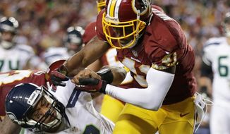 Washington Redskins free safety Madieu Williams stops Seattle Seahawks quarterback Russell Wilson during the first half of an NFL wild card playoff football game in Landover, Md., Sunday, Jan. 6, 2013. (AP Photo/Evan Vucci)