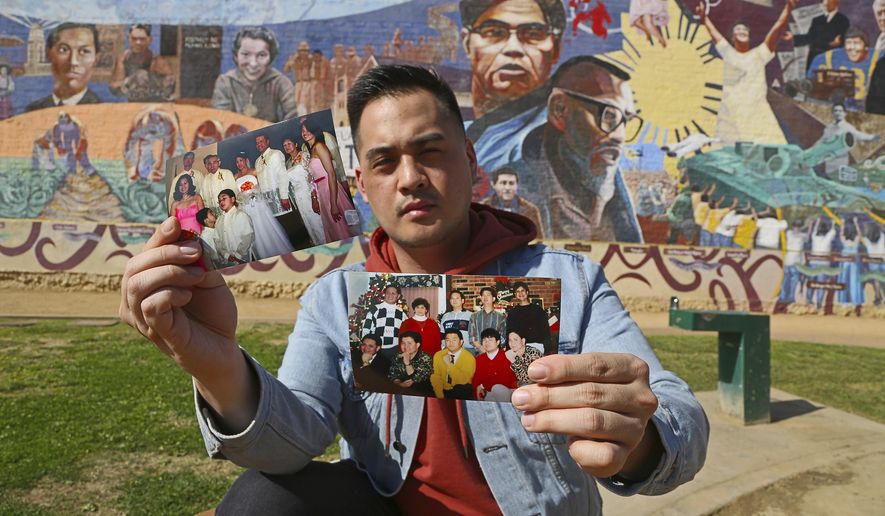 In this Thursday, Feb. 1, 2018 photo, Filipino American Jeff DeGuia, 28, holds up family pictures at Unidad (Unity) Park in Los Angeles. DeGuia, 28, says it took his mother more than a decade to bring two sisters from the Philippines. “There’s definitely this idea you are not really complete without your huge family,” said DeGuia, whose grandfather came to the United States for an engineering job in the 1970s. In the background is Eliseo Art Silva&#x27;s mural &amp;quot;Gintong Kasaysayan, Gintong Pamana,&amp;quot; A Glorious History, A Golden Legacy. (AP Photo/Reed Saxon)