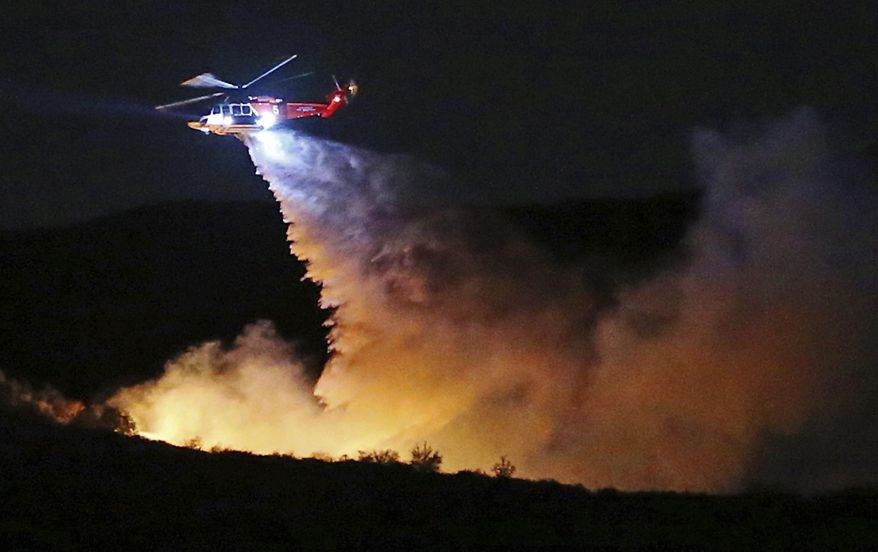 A helicopter makes a water drop on a brush fire that broke out near Temescal Ridge Trail in the vicinity of Skull Rock in a remote section of Topanga State Park in the hills above the Pacific Palisades neighborhood of Los Angeles Wednesday evening, Feb. 21, 2018. No structures are threatened and no evacuations have been called for. (AP Photo/Reed Saxon)