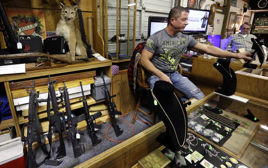 In this photo taken Oct. 20, 2017, Johnny's Auction House owner John West prepares items, including a line of assault rifles behind, for auction where the company handles gun sales for both civilians and a half dozen police departments and the Lewis County Sheriff's Office, in Rochester, Wash. When Washington state and other law enforcement agencies across the country sell guns they've confiscated during criminal investigations, they're not just selling pistols and hunting rifles, they're also putting assault weapons, including AR-15s, back on the street. (AP Photo/Elaine Thompson)
