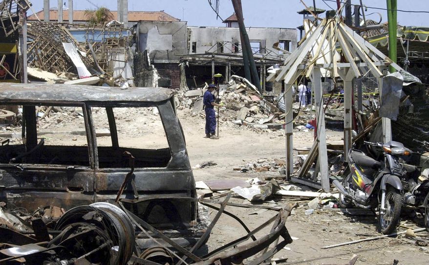 FILE - In this Oct. 21, 2002, file photo, an Australian police officer stands near the ruins of the Sari Club, background, which was flattened by a bomb attack in Kuta, Bali, Indonesia. The Indonesian government is bringing together dozens of convicted Islamic militants and survivors of attacks in what it hopes will be an important step in combating radicalism and fostering reconciliation. The three days of meetings began Monday, Feb. 26, 2018. (AP Photo/Achmad Ibrahim, File)