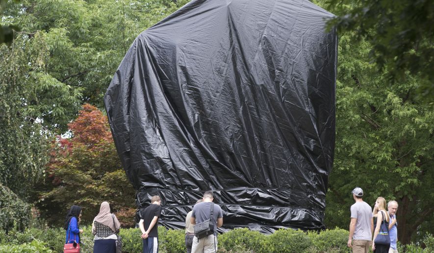 FILE - This Wednesday Aug. 23, 2017 file photo shows residents and visitors as they look over the covered statue of Confederate General Robert E. Lee in Emancipation park in Charlottesville, Va. A judge in Virginia has ordered the city of Charlottesville to remove the black shrouds that were installed over two Confederate monuments last summer after a white nationalist rally. (AP Photo/Steve Helber)