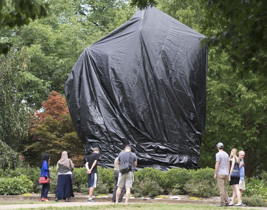 FILE - This Wednesday Aug. 23, 2017 file photo shows residents and visitors as they look over the covered statue of Confederate General Robert E. Lee in Emancipation park in Charlottesville, Va. A judge in Virginia has ordered the city of Charlottesville to remove the black shrouds that were installed over two Confederate monuments last summer after a white nationalist rally. (AP Photo/Steve Helber)