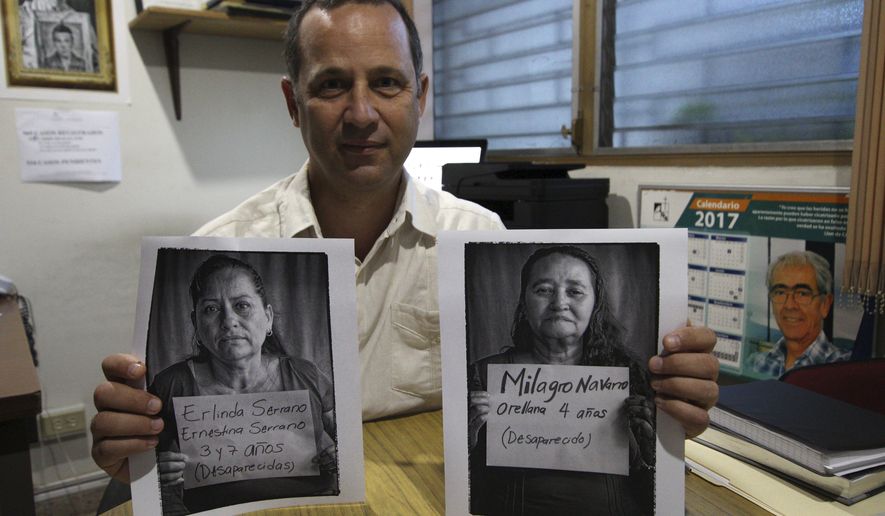 In this Feb. 16, 2018 photo, Pro-busqueda Executive Director, Eduardo Garcia, holds portraits of Salvadoran women who lost their siblings during the Civil war in El Salvador, in San Salvador, El Salvador. The photo on the right shows Emma Orellana with a sign that has the name of her sister Milagro, who disappeared in 1984 when she was 4-years-old. Her bones where found and reburied in 2017. The photo on the left shows Suyapa Serrano holding a sign with the names of her sisters Erlinda and Ernestina who disappeared in 1982 and are still missing. (AP Photo/Salvador Melendez)