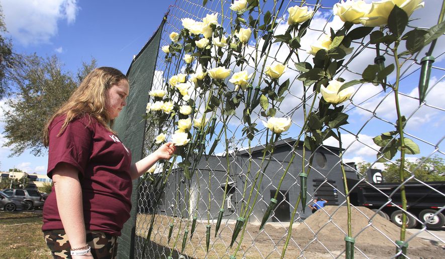 Annabel Claprood, a student at Marjory Stoneman Douglas High School touches one of the roses at the Pulse night club, Wednesday, Feb. 28, 2018 in Orlando, Fla.  Parents and students of Marjory Stoneman Douglas High School made a stop at the site of the nightclub attack  on their way back home from Tallahassee. Students returned to class at the high school, Wednesday, following the Feb. 14 mass shooting that killed several students and teachers.  (Red Huber/Orlando Sentinel via AP)