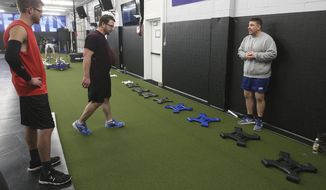 In this Jan. 24, 2018 photo, Millikin University wrestlers, Verneil Phillips, left, and Bradley  Owens, listen as wrestling coach Ryan Birt, right, gives instruction before they start using Birt Plates at the Millikin University wrestling facility in Decatur, Ill. Birt, was an NCAA Division III national wrestling champion and football player at Upper Iowa University when He injured his elbow when a helmet slammed into it, and during his rehabilitation was unable to use a straight bar to lift weights. Brit designed the Birt Plates rehab device after the injury. (Jim Bowling/Herald &amp;amp; Review via AP)