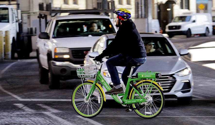 In this Feb. 22, 2018 photo, a man rides a shared electric-assisted bicycle in downtown Seattle. Shared bikes that can be left wherever the rider ends up are helping more people get access to the mode of transportation that reduces car traffic and increases exercise, but they are also producing some chaos with discarded bikes cluttering public spaces, blocking sidewalks and even placed in trees and lakes. Over the last year, startup companies have brought the bikes that can be unlocked with an app and don't require docking stations into city after city in the U.S. (AP Photo/Elaine Thompson)