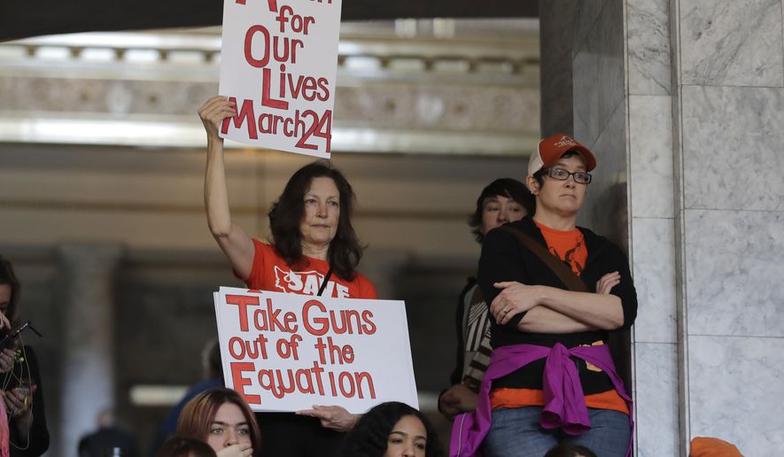 An attendee at a rally against gun violence holds signs that read &quot;March for Our Lives March 24&quot; and &quot;Take Guns Out of the Equation,&quot; Tuesday, March 6, 2018, at the Capitol in Olympia, Wash. The rally was held on the same day Gov. Inslee was scheduled to sign a bill banning the sale and possession of gun bump stocks in the state of Washington. (AP Photo/Ted S. Warren)