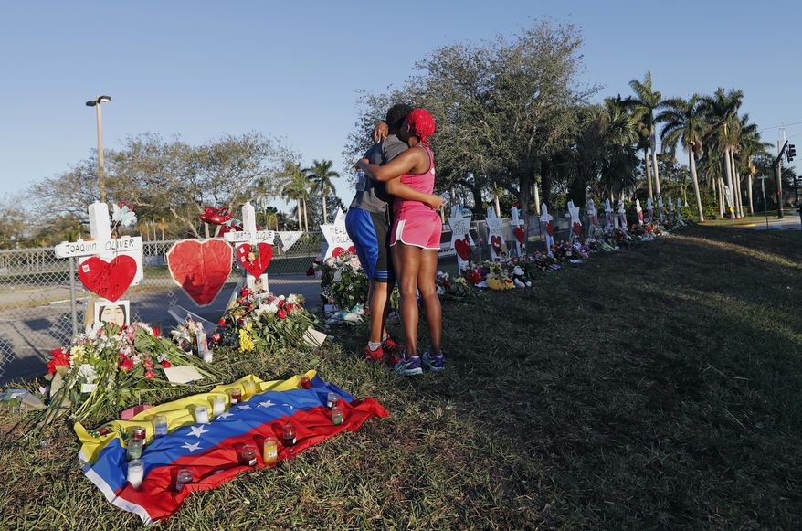This Feb. 19, 2018, file photo shows Denyse Christian, hugging her son Adin Christian, 16, a student at the school, at a makeshift memorial outside the Marjory Stoneman Douglas High School, where 17 students and faculty were killed in a mass shooting in Parkland, Fla. Parkland city’s historian Jeff Schwartz is setting a plan in motion to collect, archive and preserve the Marjory Stoneman Douglas mementos. Meanwhile, school administrators have vowed to build a memorial after the demolition of the building where the Feb. 14 attack took place. (AP Photo/Gerald Herbert, File)
