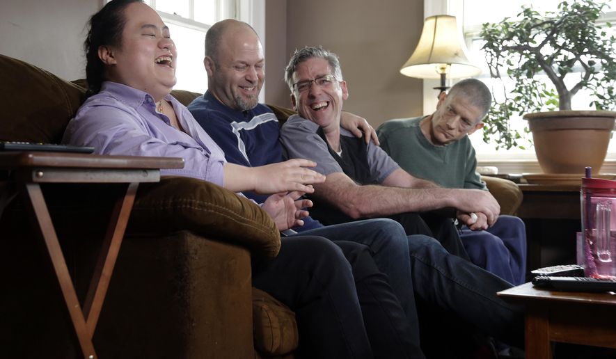 In this March 5, 2018 photo, Wil Darcangelo, second from left, and his husband, Jamie, laugh with their 22-year-old adopted daughter, Lavender, who is blind and autistic, at their home in Fitchburg, Mass. Friend and housemate, Christoph Malvaney, who suffers from stroke and other ailments, listens at far right. "Chosen families" have quietly been gaining political recognition in some laws that require paid sick time for millions of private-sector employees to take care of themselves or family members. (AP Photo/Elise Amendola)