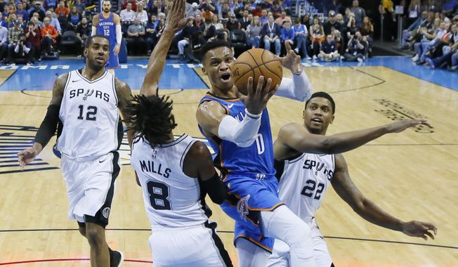 Oklahoma City Thunder guard Russell Westbrook (0) goes to the basket between San Antonio Spurs guard Patty Mills (8) and forward Rudy Gay (22) in the first half of an NBA basketball game in Oklahoma City, Saturday, March 10, 2018. (AP Photo/Sue Ogrocki)