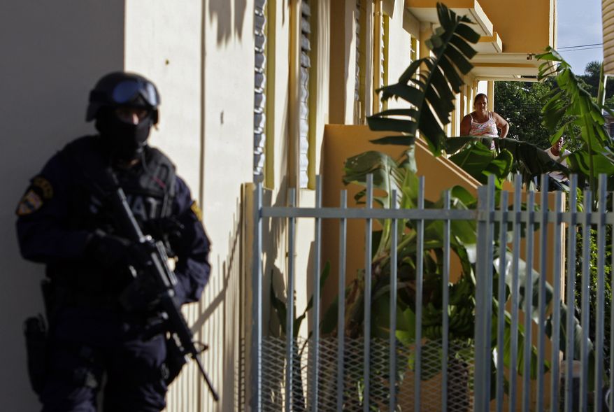 A resident of a public housing project (behind right) watches police conduct an anti-drug raid in Mayaguez, Puerto Rico, on July 9, 2010. (Associated Press) **FILE**