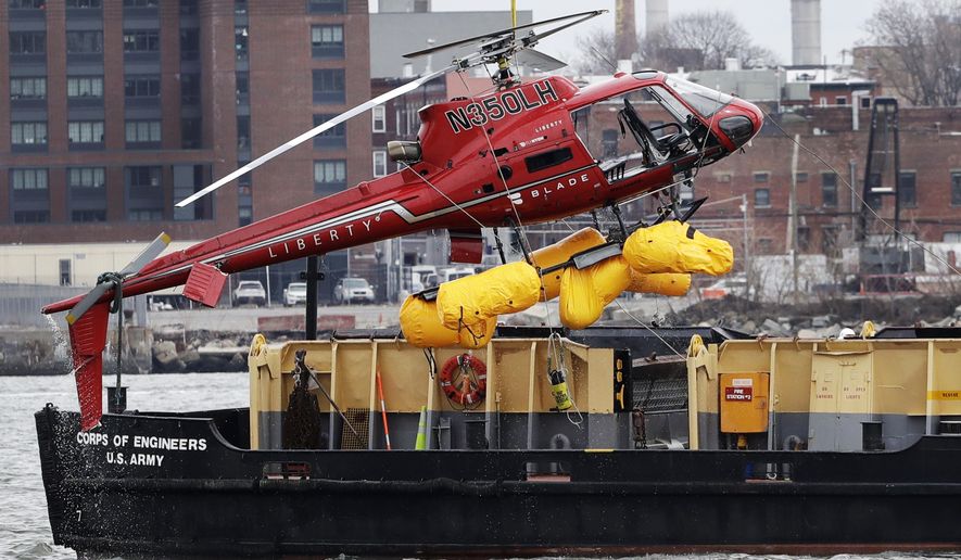 A helicopter is hoisted by crane from the East River onto a barge, Monday, March 12, 2018, in New York. The pilot was able to escape the Sunday night crash after the aircraft flipped upside down in the water killing several passengers, officials said. (AP Photo/Mark Lennihan)