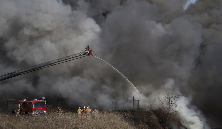 A large, black plume of smoke rises into the sky in Northeast Portland on Monday, March 12, 2018, as a pile of scrap cars burns in the area of 75th Avenue and Killingsworth Street. The fire eventually spread to a nearby apartment building and duplex, burning some units. (Dave Killen/The Oregonian via AP)