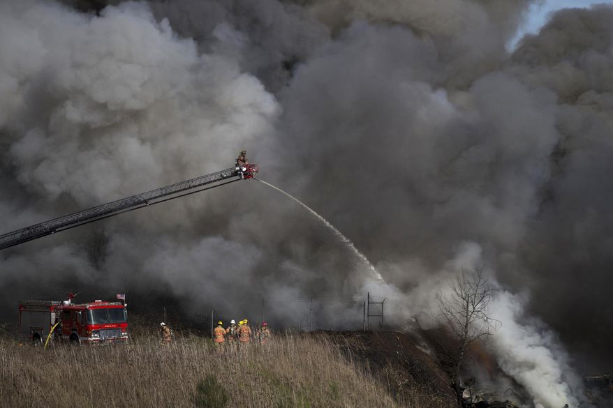 A large, black plume of smoke rises into the sky in Northeast Portland on Monday, March 12, 2018, as a pile of scrap cars burns in the area of 75th Avenue and Killingsworth Street. The fire eventually spread to a nearby apartment building and duplex, burning some units. (Dave Killen/The Oregonian via AP)
