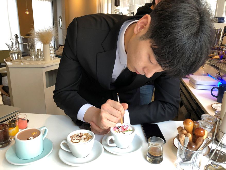 In this March 1, 2018, photo, Barista Lee Kang Bin applies the finishing touches to a recreation of a couple's Niagara Falls vacation photo, at his coffee shop in Seoul, South Korea. The South Korean barista is charming customers at his coffee shop by drawing intricate artworks on the foamy cream toppings of their drinks. (AP Photo/Dino Hazell)