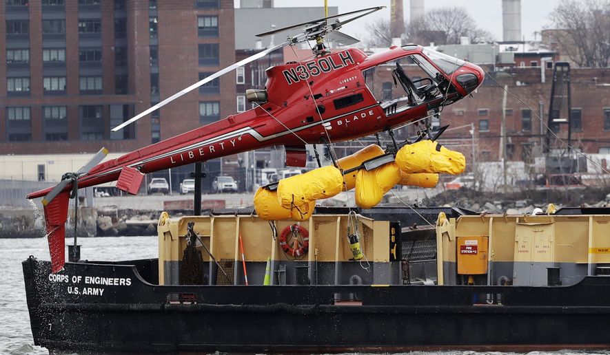 FILE - In this March 12, 2018 file photo, a helicopter is hoisted by crane from the East River onto a barge in New York after a Sunday night crash.  The crash is prompting regulators to temporarily ground “doors off” flights using tight restraints that could trap people in an emergency. The Federal Aviation Administration ordered the ban on Friday amid concerns such harnesses prevented passengers from escaping. Five people were killed. (AP Photo/Mark Lennihan, File)